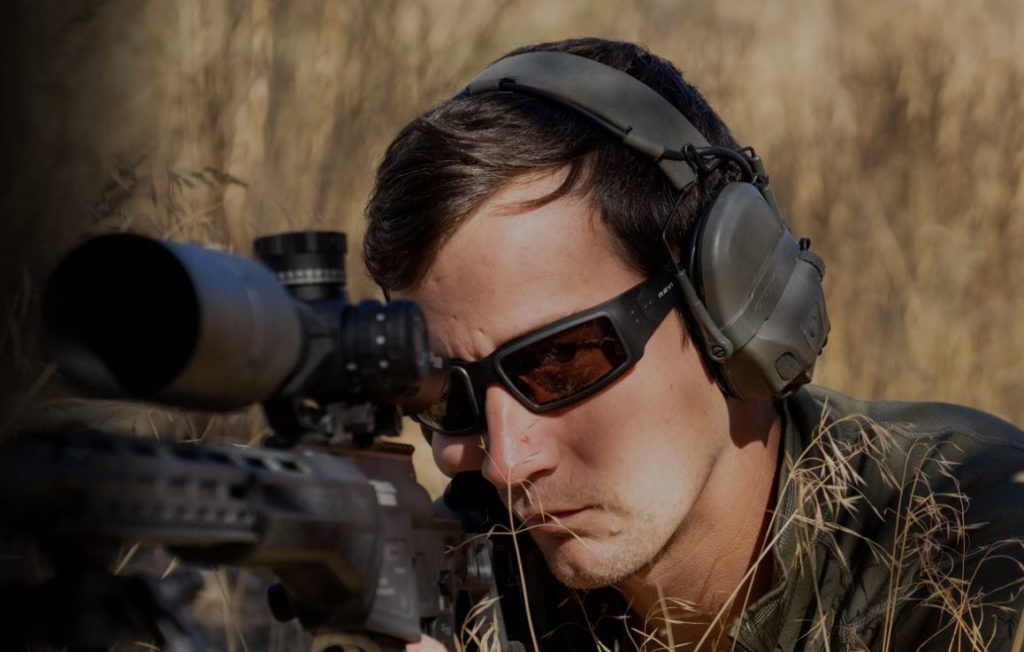 Man holding a rifle and wearing Revision's aluminum eyewear