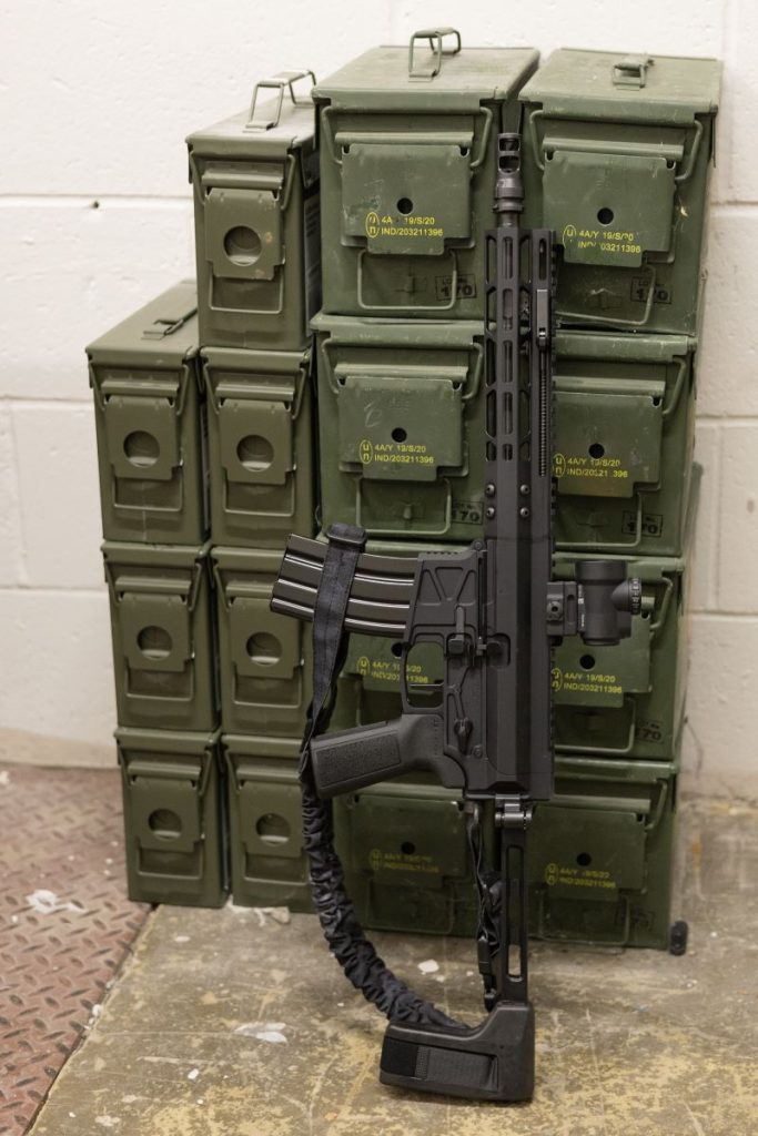 Monolith rifle leaning against green containers.